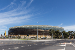 Ein großes Stadion mit starkem Verkehr davor, umgeben von Straßenmasten, Laternen, Verkehrszeichen, Schildern, Geländern, Bäumen und einem bewölkten Himmel.