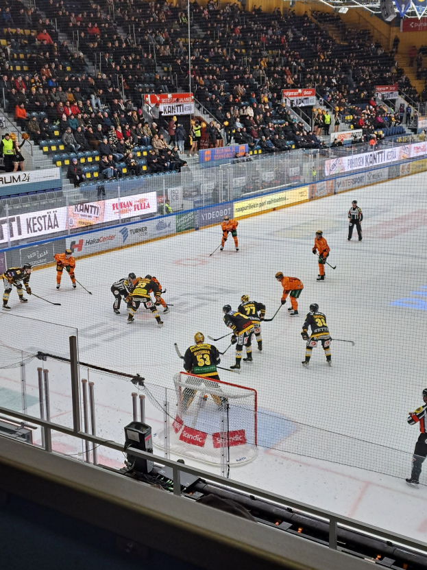 Eine Gruppe von Menschen, die Hockey auf einem Eisstadion spielen, mit Zuschauern im Hintergrund und Schildern.