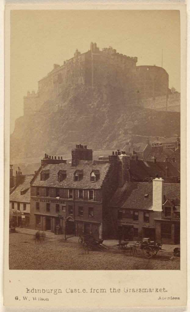 Alte Fotografie von Edinburgh Castle von Grassmarket aus betrachtet, mit Gebäuden und Wagen im Vordergrund und einem Hügel im Hintergrund, mit Text am unteren Rand.
