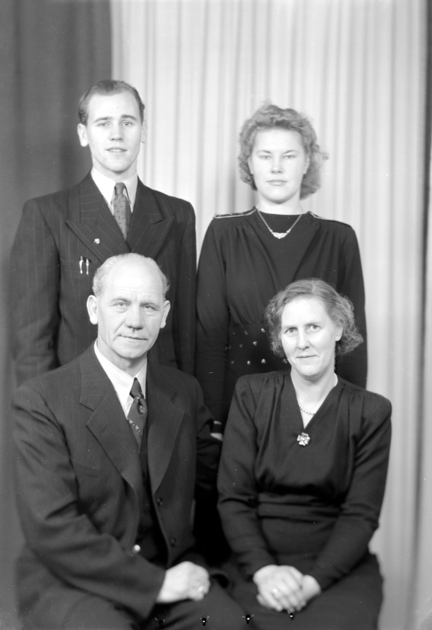 Ein Schwarz-Weiß-Foto von vier Menschen in Anzügen vor einem Vorhang.