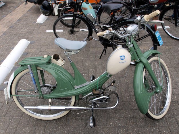 Ein grüner Moped mit weißem Rahmen und schwarzem Sitz neben anderen Motorrädern auf einem Gehweg geparkt, mit einigen Menschen in der Nähe.